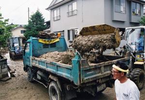 ショベルカーを使い、道路に積もった汚泥を排除するトラックの写真