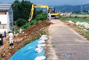 クレーン車を使い、決壊箇所対岸の田島二丁目地内右岸堤防修復作業様子の写真
