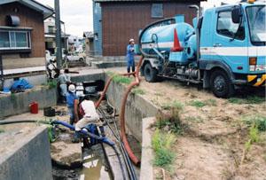 水路に溜まった泥を吸い上げるバキュームカーの写真