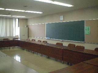 ロの字型に長机が並べられて黒板がある会議室の写真