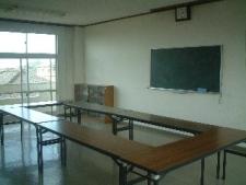 ロの字に並べられた長机、黒板のある講義室の写真