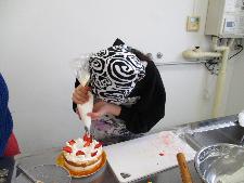 調理台の上でイチゴと生クリームのクリスマスケーキをホイップしている女の子