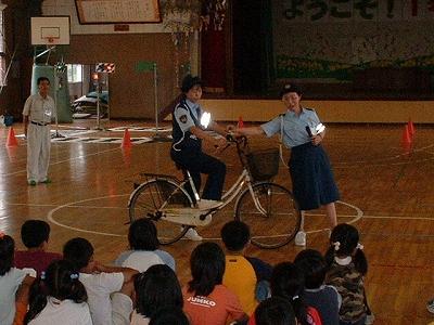 小学校の体育館にて婦警さんたちが自転車運転の指導をしている写真