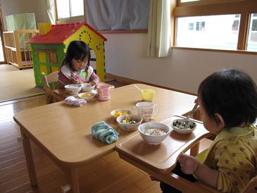 子ども2人が椅子に座って向かい合せでご飯を食べている写真